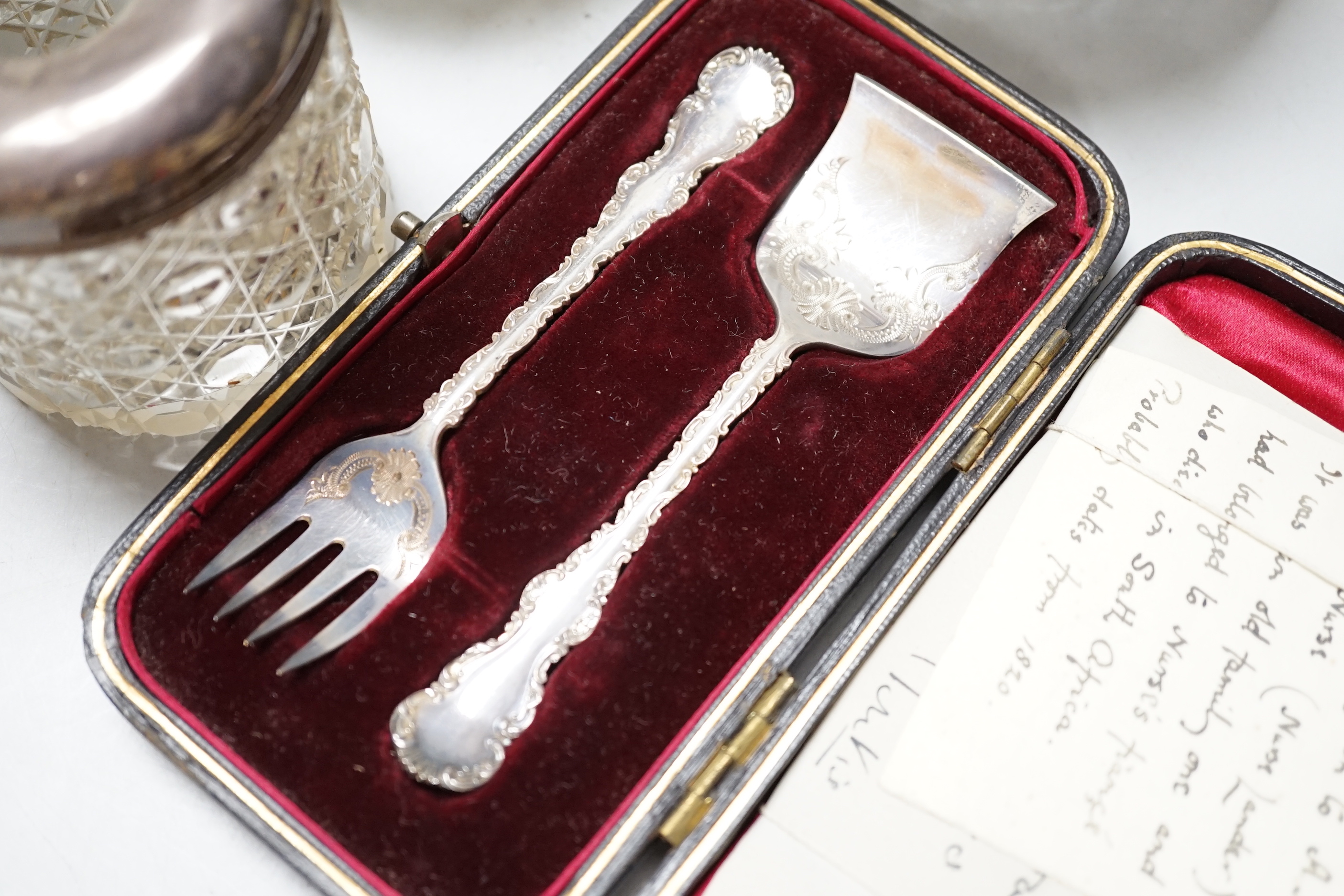 A pair of George V silver mounted cut glass scent bottles, London 1920, 11cm, a similar toilet jar, a hair tidy and a cased two piece christening set